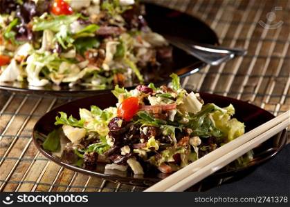 Fresh chopped salad on a black plate with chop sticks in the foreground. Salad serving dish in the background.