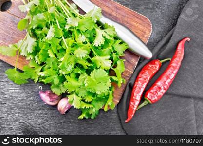 Fresh cilantro, knife, garlic, hot red pepper and napkin against a wooden board background from above