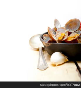 fresh clams stewed on an iron skillet over wite rustic wood table