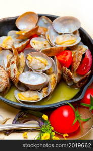 fresh clams stewed on an iron skillet over wite rustic wood table