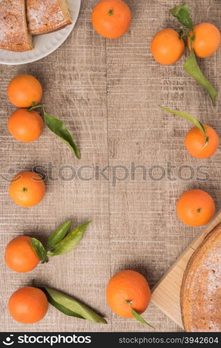 Fresh clementines and cake on wooden board with leaves. Top view with copy space.