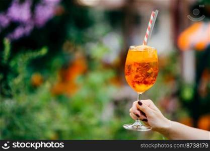 Fresh cocktail in wine glass outdoor against blurred background. Woman holds summer cold drink with ice. Horizontal shot. Tasty acoholic beverage