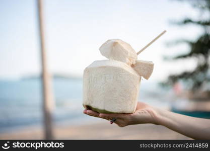 Fresh coconut cocktail in hand over ocean background.