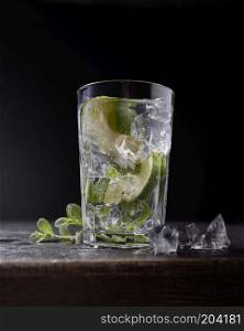Fresh cold water with lime, mint and ice in a glass on dark stone background. Delicious refreshing lemonade with ice and mint on dark