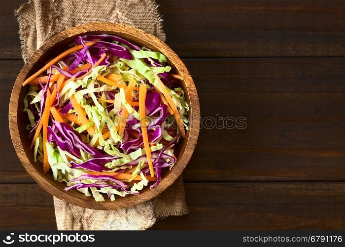 Fresh coleslaw, a salad made of shredded red and white cabbage and carrots, served in wooden bowl, photographed overhead on dark wood with natural light (Selective Focus, Focus on the top of the salad)