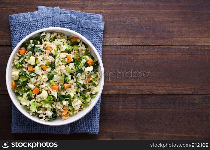 Fresh cooked brown rice with steamed vegetables (broccoli, cauliflower, swiss chard, carrot, celery) in bowl, photographed overhead with copy space on the right side . Brown Rice with Vegetables