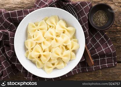 Fresh cooked farfalle, bow-tie or butterfly pasta served in bowl without sauce, ground black pepper on the side, photographed overhead. Cooked Farfalle Pasta