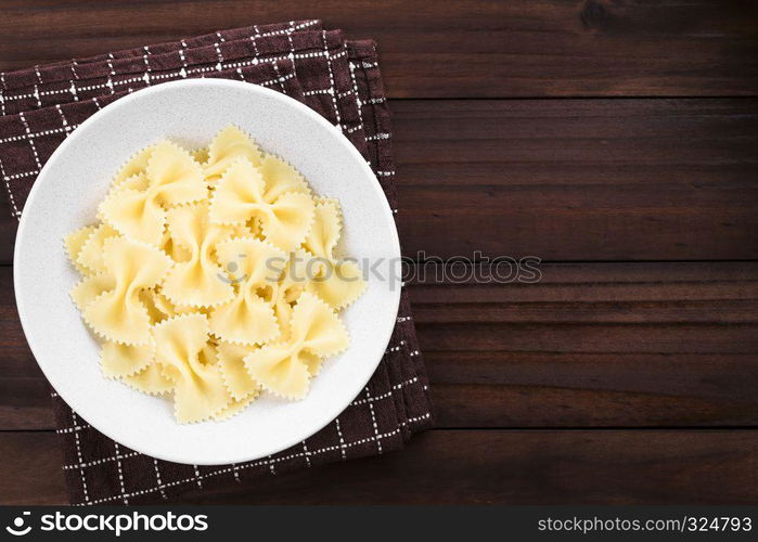 Fresh cooked farfalle, bow-tie or butterfly pasta served in bowl without sauce, photographed with copy space overhead on dark wood. Cooked Farfalle Pasta