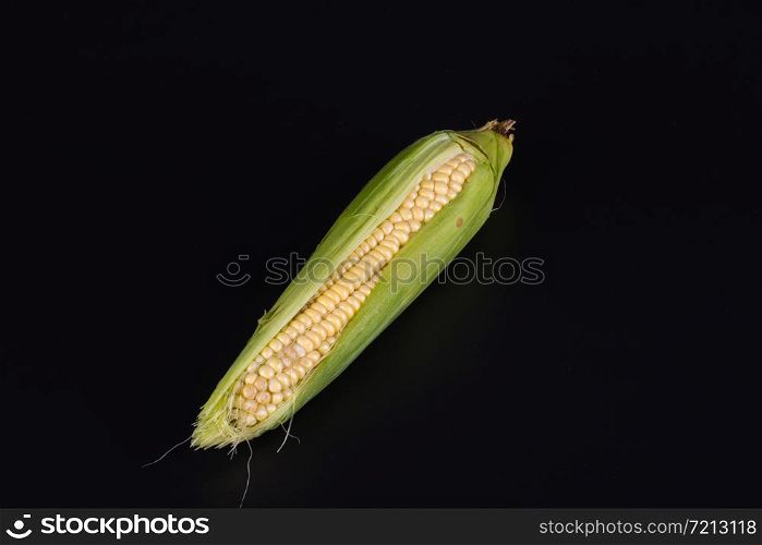 fresh corn in green husk lies on a black background, top view. one corn husk