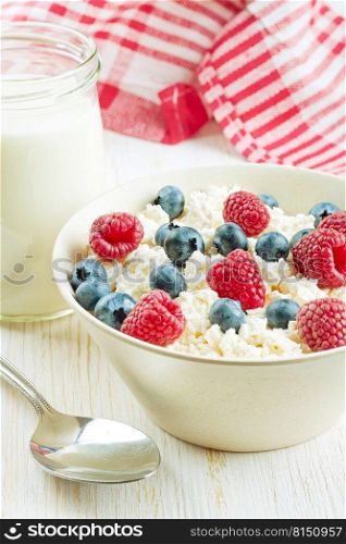 Fresh cottage cheese with berries in white bowl and jar of milk on white wooden background. cottage cheese with berries