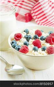 Fresh cottage cheese with berries in white bowl and jar of milk on white wooden background. cottage cheese with berries