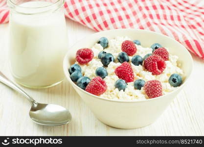 Fresh cottage cheese with berries in white bowl and jar of milk on white wooden background. cottage cheese with berries