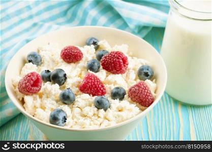 Fresh cottage cheese with raspberries and blueberries in white bowl on blue wooden background. Cottage cheese with berries in white bowl on blue wooden background