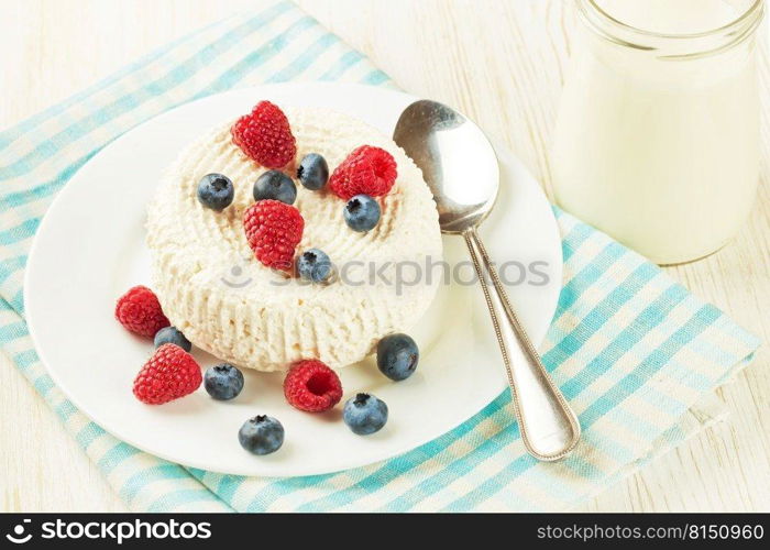 Fresh cottage cheese with raspberries and blueberries on white plate. Cottage cheese with berries on white background