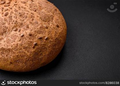 Fresh crispy brown bread with sesame seeds and spices on a dark concrete background