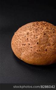 Fresh crispy brown bread with sesame seeds and spices on a dark concrete background