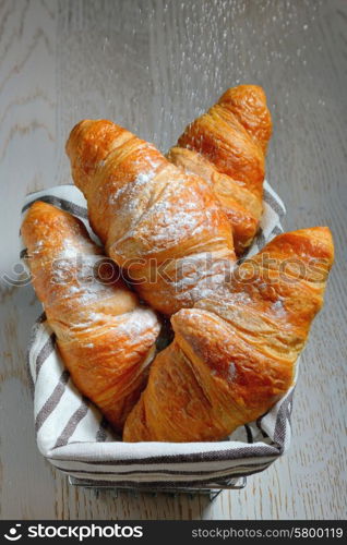 fresh croissants in basket on wooden table