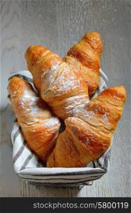 fresh croissants in basket on wooden table