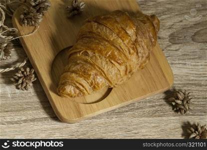 Fresh croissants placed on a wooden cutting board on a wooden table ready to eat from the top view