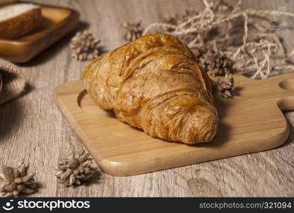 Fresh croissants placed on a wooden cutting board on a wooden table ready to eat