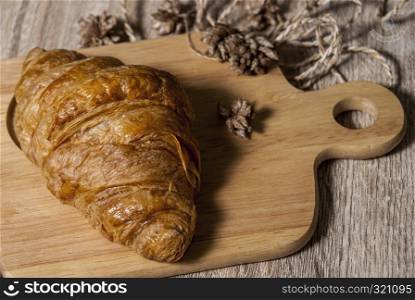 Fresh croissants placed on a wooden cutting board on a wooden table ready to eat