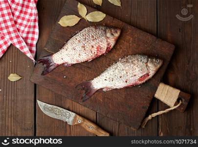 fresh crucian fish sprinkled with spices lies on a brown wooden cutting board, wooden table from boards, top view