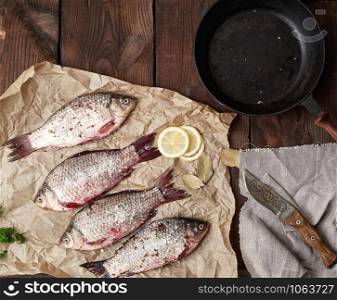 fresh crucian fish sprinkled with spices lies on brown crumpled paper, wooden table from boards, top view