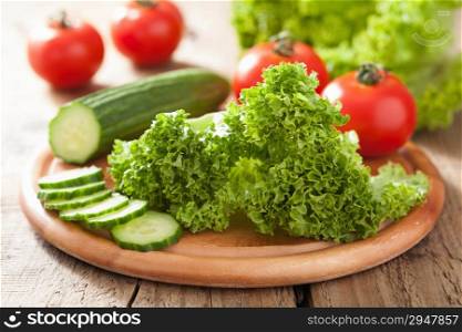 fresh cucumber tomatoes and salad leaves on chopping board