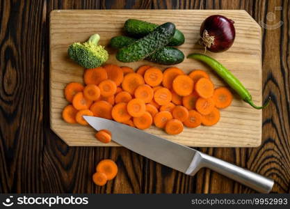 Fresh cutted vegetables on board and knife isolated on wooden background. Organic vegetarian food, grocery assortment, natural eco products, healthy lifestyle concept. Cutted vegetables and knife, wooden background