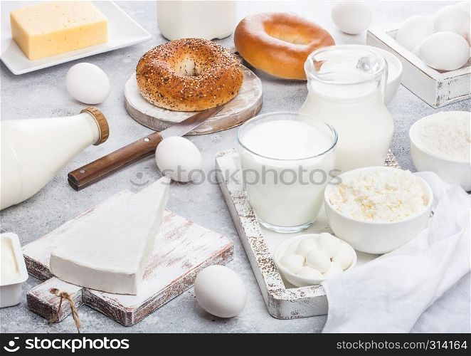 Fresh dairy products in vintage wooden box on white background. Jar and glass of milk, bowl of sour cream and cheese and eggs. Fresh baked bagel on round chopping board with knife.