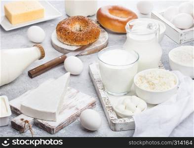 Fresh dairy products in vintage wooden box on white background. Jar and glass of milk, bowl of sour cream and cheese and eggs. Fresh baked bagel on round chopping board with knife.