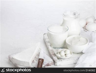 Fresh dairy products in vintage wooden box on white table background. Jar and glass of milk, bowl of sour cream and cheese.