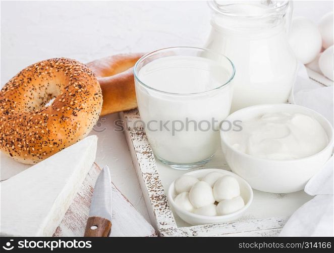 Fresh dairy products in vintage wooden box on white table background. Jar and glass of milk, bowl of sour cream and cheese. Fresh baked bagels.
