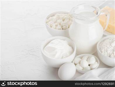 Fresh dairy products on white background. Glass jar of milk, bowl of sour cream, cottage cheese and baking flour and mozzarella. Eggs and cheese.