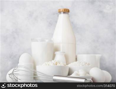 Fresh dairy products on white background. Glass jar of milk, bowl of sour cream, cottage cheese and baking flour and mozzarella. Eggs and cheese. Steel whisk