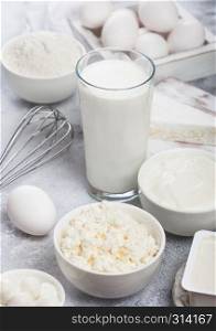 Fresh dairy products on white background. Glass of milk, bowl of sour cream and cottage cheese and eggs in wooden box. Steel whisk.