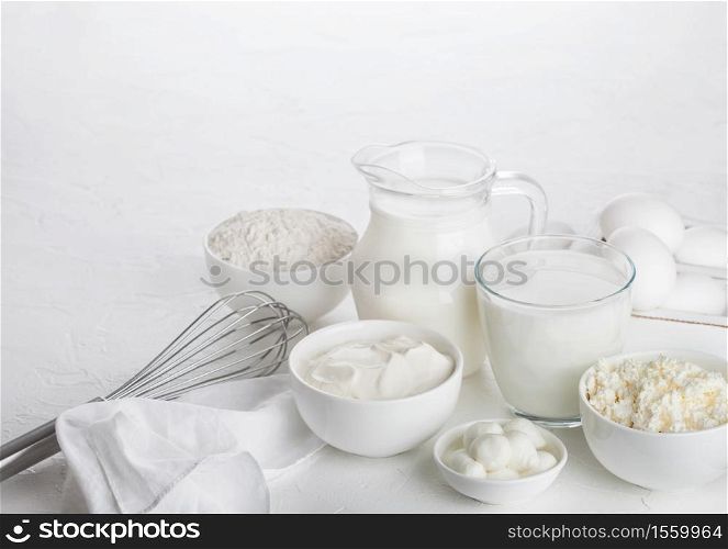 Fresh dairy products on white background. Jar and glass of milk, bowl of sour cream, cottage cheese and baking flour and mozzarella. Eggs and cheese.