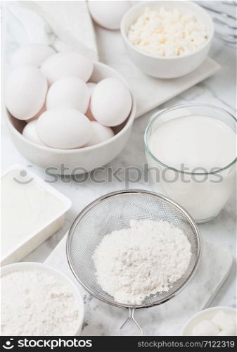 Fresh dairy products on white marble background. Glass of milk, bowl of flour, sour cream and cottage cheese and eggs. Steel whisk