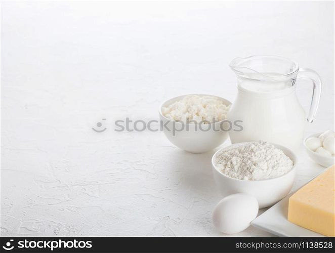 Fresh dairy products on white table background. Glass jar of milk, bowl of cottage cheese and baking flour. Eggs and cheese.