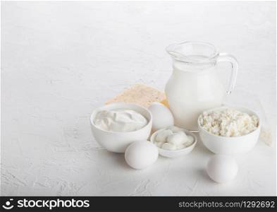 Fresh dairy products on white table background. Glass jar of milk, bowl of sour cream and cottage cheese and mozzarella. Eggs in and cheese.