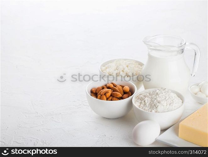 Fresh dairy products on white table background. Glass jar of milk, bowl of cottage cheese and baking flour and almond nuts. Eggs and cheese.