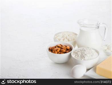 Fresh dairy products on white table background. Glass jar of milk, bowl of cottage cheese and baking flour and almond nuts. Eggs and cheese.
