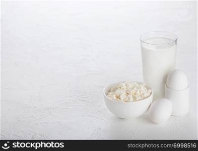 Fresh dairy products on white table background. Glass of milk, bowl cottage cheese and eggs.