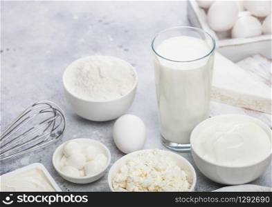 Fresh dairy products on white table background. Glass of milk, bowl of sour cream, cottage cheese and baking flour and mozzarella. Eggs and cheese. Steel whisk
