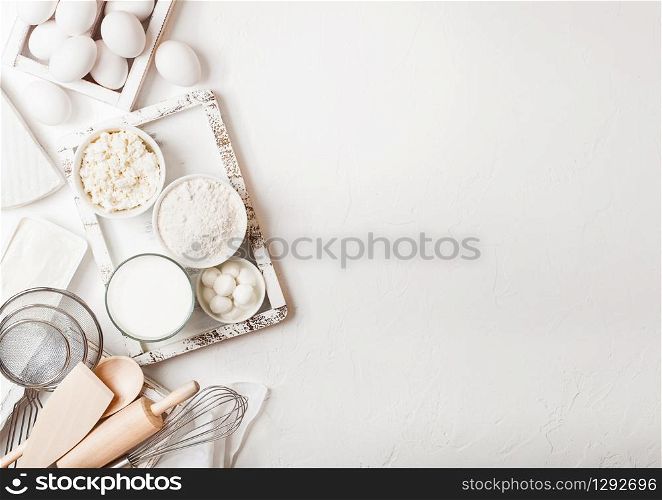Fresh dairy products on white table background. Glass of milk, bowl of flour and cottage cheese and eggs. Box of baking utensils. whisk and spatula in vintage wooden box.Top view.