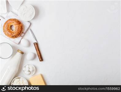 Fresh dairy products on white table background. Glass of milk, bowl of sour cream and cottage cheese and eggs. Fresh baked bagel. Steel whisk. Top view.