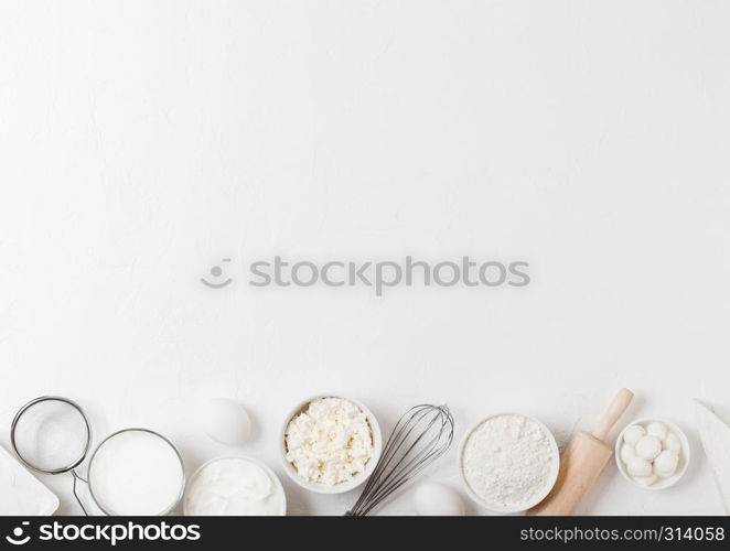 Fresh dairy products on white table background. Glass of milk, bowl of flour, sour cream and cottage cheese and eggs. Steel whisk and rolling pin.