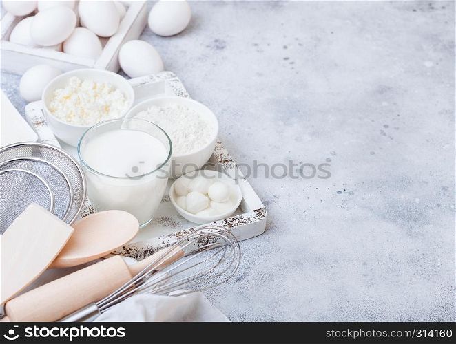 Fresh dairy products on white table background. Glass of milk, bowl of flour and cottage cheese and eggs. Box of baking utensils. whisk and spatula in vintage wooden box.Top view.