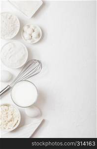 Fresh dairy products on white table background. Glass of milk, bowl of flour, sour cream and cottage cheese and eggs. Steel whisk