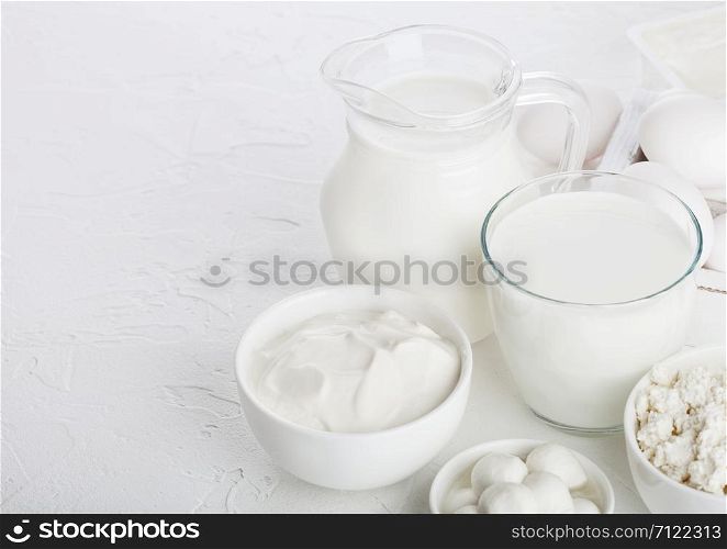 Fresh dairy products on white table background. Jar and glass of milk, bowl of sour cream, cottage cheese and mozzarella. Eggs in wooden box. Space for text